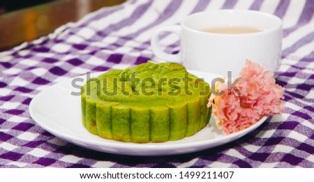 Food photography, Closeup side view picture of sticky rice, matcha moon cake on a white plate with decorative flower and a cup of ginger tea. This is a traditional mid autumn snack