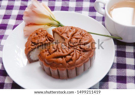 Food photography, top down view Closeup picture of a baked moon cake, with a piece cut out on a white plate with a cup of ginger tea. This is a traditional mid autumn snack