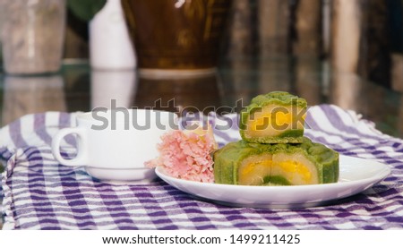 Food photography, Closeup picture of sticky rice, matcha moon cake filled with salted egg on a white plate with decorative flower and a cup of ginger tea. This is a traditional mid autumn cake