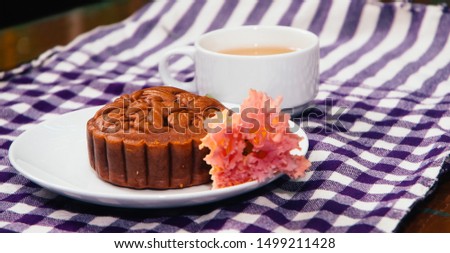Food photography, side view Closeup picture of a baked moon cake on a white plate with a cup of ginger tea on a blue checkered table cloth. This is a traditional mid autumn snack