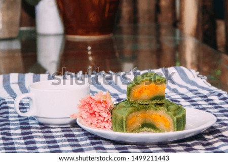 Food photography, Closeup picture of sticky rice, matcha moon cake filled with salted egg on a white plate with decorative flower and a cup of ginger tea. This is a traditional mid autumn snack