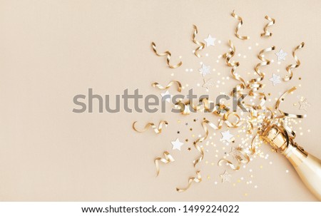 Champagne bottle with confetti stars and party streamers on gold festive background. Christmas, birthday or wedding concept. Flat lay.