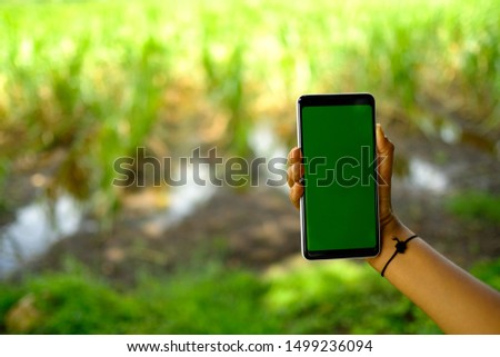 A Indian kid holding smartphone with farm in the background