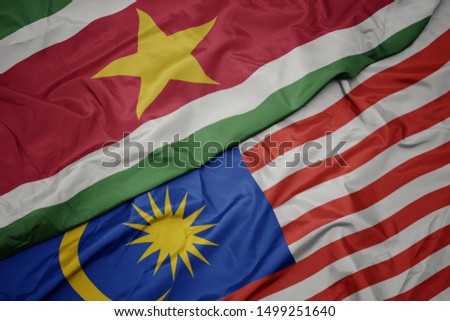 waving colorful flag of malaysia and national flag of suriname. macro