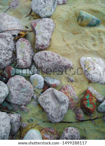 Vertical picture of a lot of rocks of different colors on the sand in a beach. Background