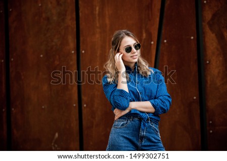 Portrait of a happy girl listening music on line with headphones from a smartphone in the street in a summer sunny day. Woman listening to music with the phone and having fun.