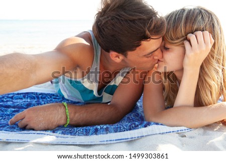 Beautiful couple on beach summer holiday together kissing in sunny vacation destination, tourists sunbathing outdoors. People using smartphone to take selfies photos, fun travel leisure lifestyle.
