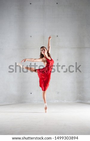 Beautiful female performer contemporary dancer lifting leg effortless on stage with harmony, body shape movement, flexibility indoors. Woman in red, motion balance conceptual lightness, lifestyle.