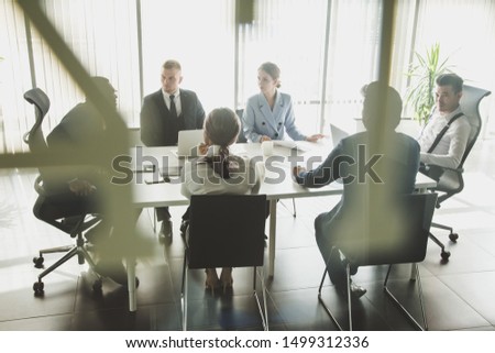 Silhouettes of people sitting at the table. A team of young businessmen working and communicating together in an office. Corporate businessteam and manager in a meeting Royalty-Free Stock Photo #1499312336
