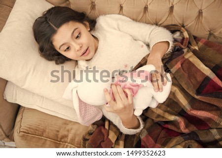Kid lay bed and hug bunny toy couch pillow blanket background top view. Girl child wear pajamas hug bunny. Play soft toy before go sleep. Sleep with toy. Girl enjoy evening time with favorite toy.