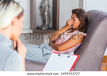 Young woman sitting on the sofa covering her face with hands, feeling hopeless, depressed or crying, visiting psychotherapist, finding out bad diagnosis or medical test results