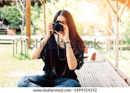 Asian female solo traveller wearing casual clothing takes a photo with DSLR professional camera