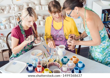 Teacher showing two women in workshop how to paint self-made dishes Royalty-Free Stock Photo #1499368637