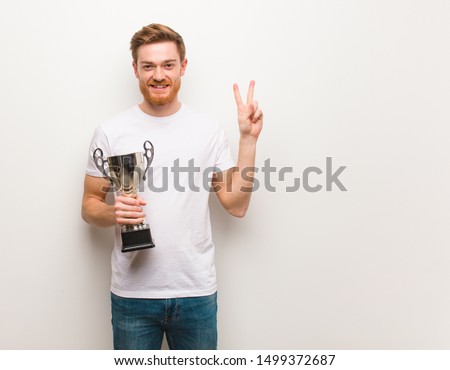 Young redhead man fun and happy doing a gesture of victory. Holding a trophy.