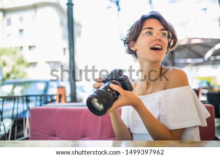 Young smiling woman look at pictures with a camera of outdoor cafe