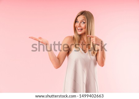 Image closeup of attractive blond woman smiling and pointing fingers at copyspace on her palm isolated over pink background
