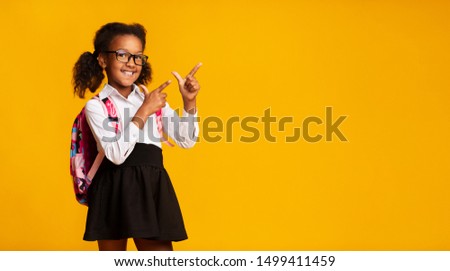 Look There. Black Elementary Student Girl Pointing Fingers At Copy Space Over Yellow Background. Panorama, Studio Shot Royalty-Free Stock Photo #1499411459