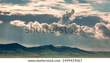 Grass hills on horizon in steppe under heavy clouds sky during sunset with sun light beams at Khakassia, Siberia, Russia.