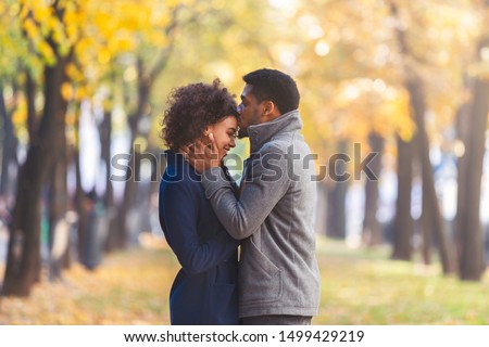 African american young man kissing his girlfriend forehead while walking in autumn city park, copy space Royalty-Free Stock Photo #1499429219