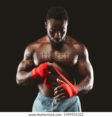 Strong african american man wrapping hands with boxing wraps, black background