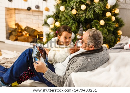 The granddaughter and a grandfather watch a photo album near the christmas tree