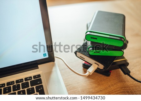 Many external hard drives on wooden table next to laptop computer, busy working photographer