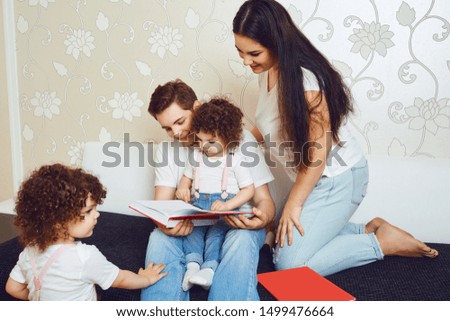 Mother and father with children read a book while sitting on a sofa in the room.