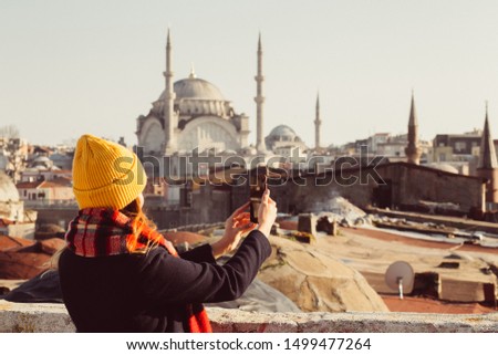 Blond woman makes photo on the phone on the roof of the Grand Bazaar, Istanbul, Turkey. Girl in a yellow hat takes a selfie on a sunny autumn day. Traveler girl walks through winter Istanbul.