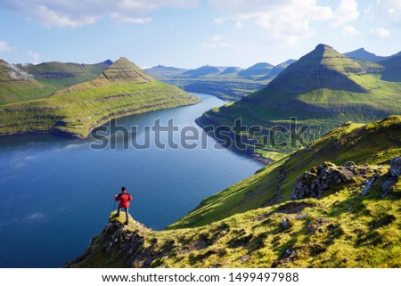 View on Funningur fjord from the Funningur top. Eysturoy Island, Faroe islands. Tourist in a red jacket explores natural attractions. Summer mountain landscape Royalty-Free Stock Photo #1499497988