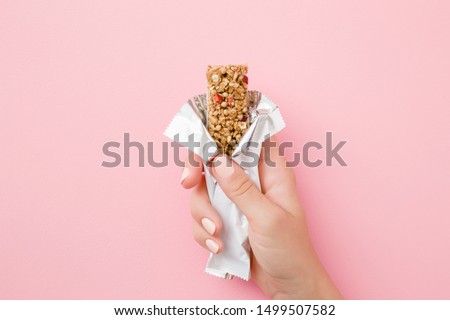 Young woman hand holding cereal bar on pastel pink table. Opened white pack. Closeup. Sweet healthy food. Royalty-Free Stock Photo #1499507582