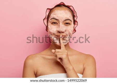 Horizontal view of pretty Asian lady with foam on face, cleans from dirt, wants to have refreshed look, makes silence gesture, wears showercap, looks happily at camera. Cleanliness and hygiene concept Royalty-Free Stock Photo #1499522069