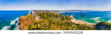 White stone Byron Bay lighthouse on the top of sandstone headland of Australian mainland the most eastern point in aerial panorama towards continent. Royalty-Free Stock Photo #1499543528