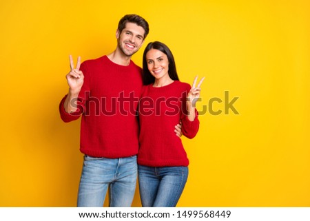 Portrait of cheerful couple make v-signs wear red pullover isolated over yellow background