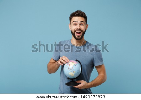 Young excited cheerful man in casual clothes posing isolated on blue wall background, studio portrait. People sincere emotions lifestyle concept. Mock up copy space. Holding in hands world globe