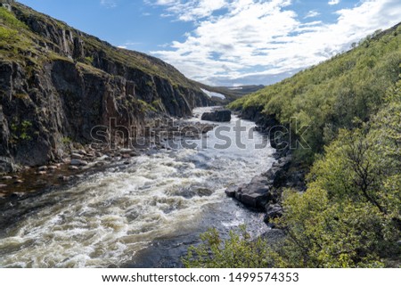 the fast Northern river with stones at the bottom flows among high rocks in the tundra