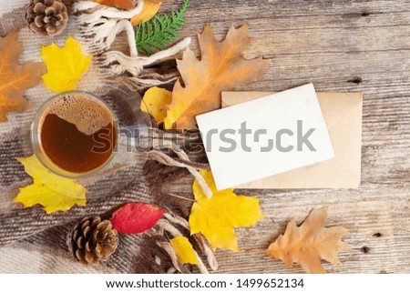 white empty card fall invitation, leaves and coffee on wooden autumn background with copy space on white paper note