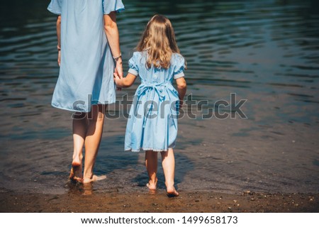 Mother and little daughter barefoot walk in the water on a river. Back view. Closeup photo