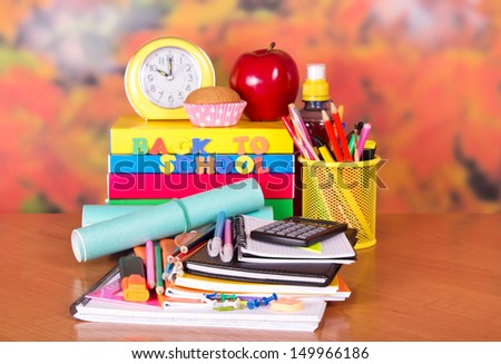 A set of school accessories, a alarm clock, a cake, apple and drink on a table