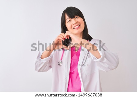 Young beautiful chinese doctor woman wearing stethoscope over isolated white background smiling in love showing heart symbol and shape with hands. Romantic concept.