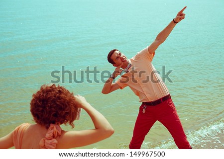Happy vacation concept. Young happy married hipsters in trendy vintage clothes making photographs (pictures) on the beach. Sunny summer day. Retro style. Copy-space. Outdoor shot