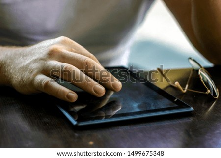 Black tablet with a blank screen in the hands on wooden table. Man hands using digital tablet with empty blank screen for text message,person browsing internet,connecting to wireless via touchscreen.