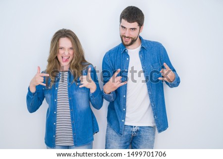 Young beautiful couple standing together over white isolated background shouting with crazy expression doing rock symbol with hands up. Music star. Heavy concept.