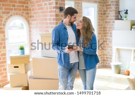 Young couple moving to a new house using smartphone around cardboard boxes