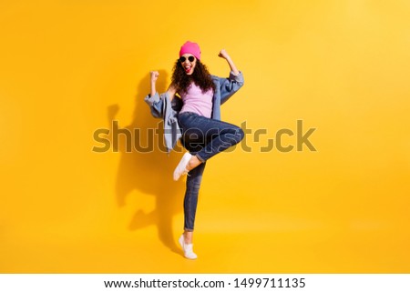 Full length photo of funny funky enthusiastic lady raise her fists scream yeah celebrate victory wear denim jeans jacket pink headwear sneakers  modern look isolated over yellow color background