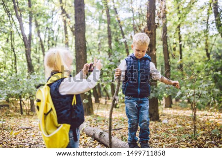 Children preschoolers Caucasian brother and sister take pictures of each other on mobile phone camera in forest park autumn. theme of hobby and active lifestyle for child. Profession photographer.