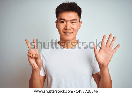 Young asian chinese man wearing t-shirt standing over isolated white background showing and pointing up with fingers number seven while smiling confident and happy.