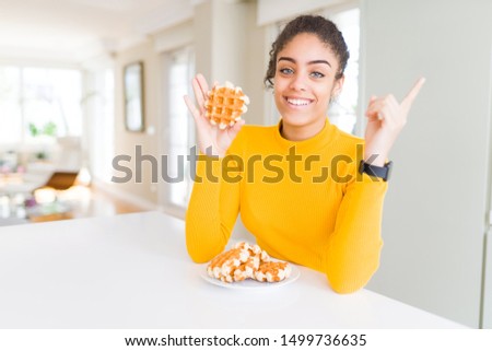 Young african american woman eating waffle belgiam pastry very happy pointing with hand and finger to the side
