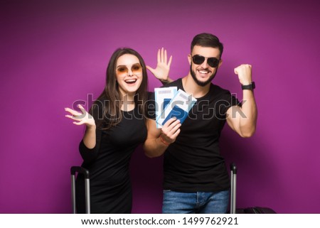 Portrait of successful lucky couple getting visa abroad holding raised fist showing passport with flying tickets shouting with wide open mouth isolated on violet background. Weekend.