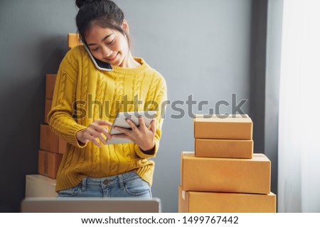 Startup small business SME, Entrepreneur owner using smartphone or tablet taking receive and checking online purchase shopping order to preparing pack product box. Selling online ideas concept Royalty-Free Stock Photo #1499767442