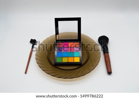 makeup brushes and shadows lie on a plate with a white background